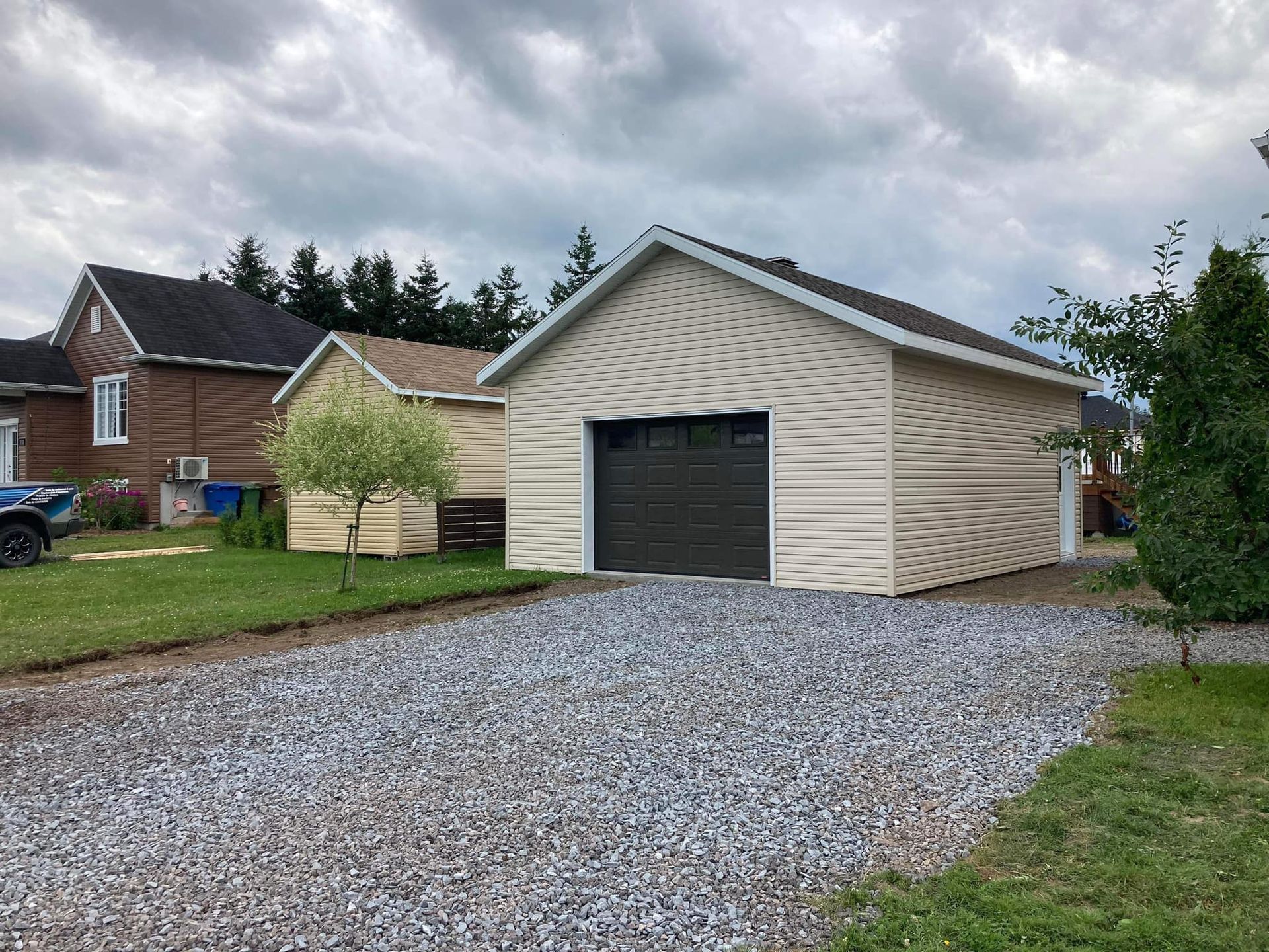 Un garage avec une porte de garage noire se trouve à côté d'une allée de gravier.
