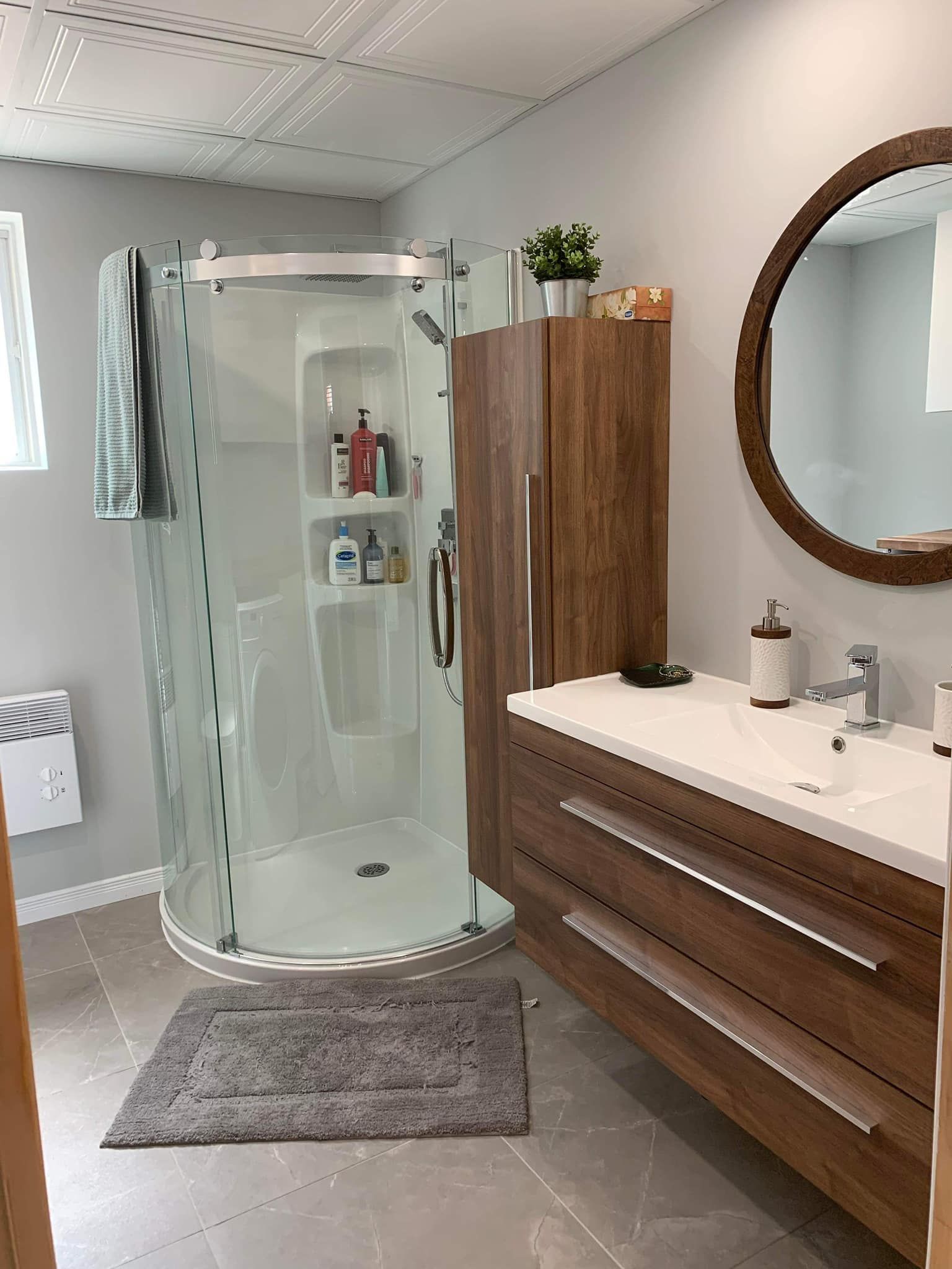 Une salle de bain avec douche, lavabo, miroir et armoires.