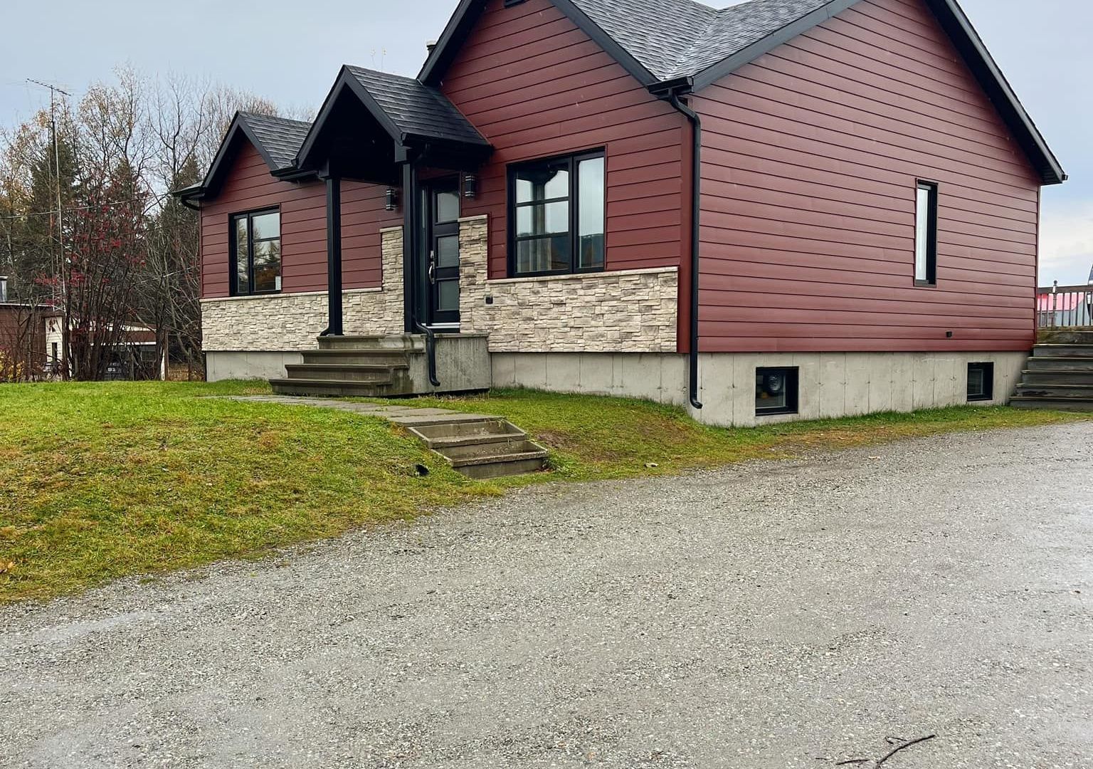 Une maison rouge avec un toit noir est assise au sommet d'une colline herbeuse.