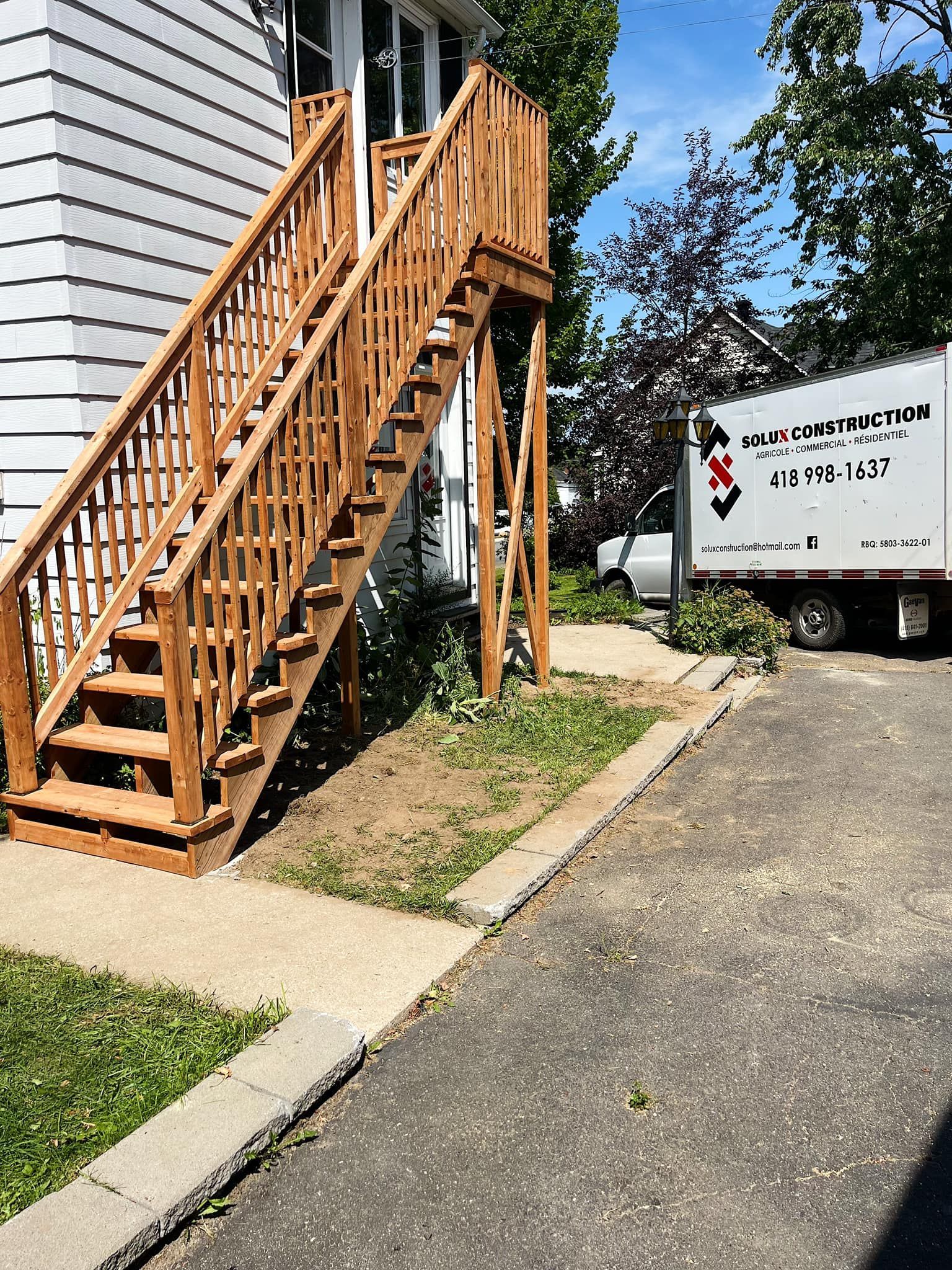 Un camion blanc est garé devant une maison avec des escaliers en bois.