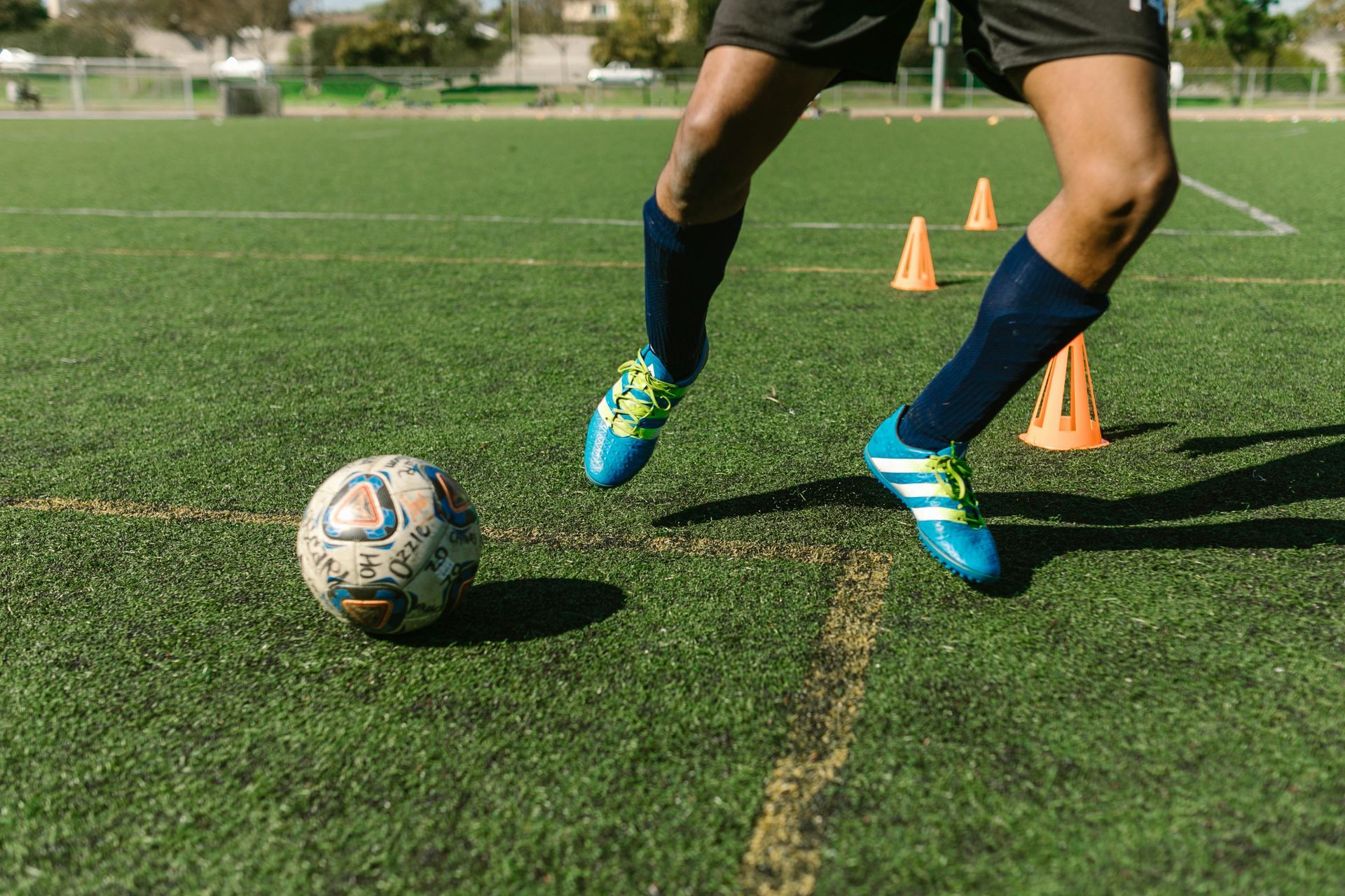 Soccer player dribbling a ball on a green field with orange cones in the background.