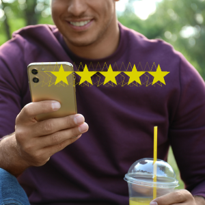 A smiling person in a purple shirt uses a smartphone to give a five-star rating while holding a drink.