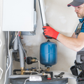 Technician wearing protective gear and red gloves performs maintenance on a residential boiler system.