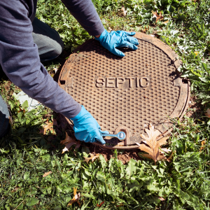 A person in blue nitrile gloves uses a wrench to open a round, heavy-duty iron cover labeled 