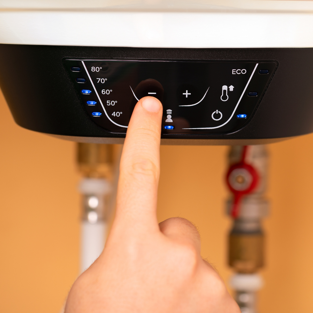 A finger presses the minus button on the digital control panel of a wall-mounted electric water heater.