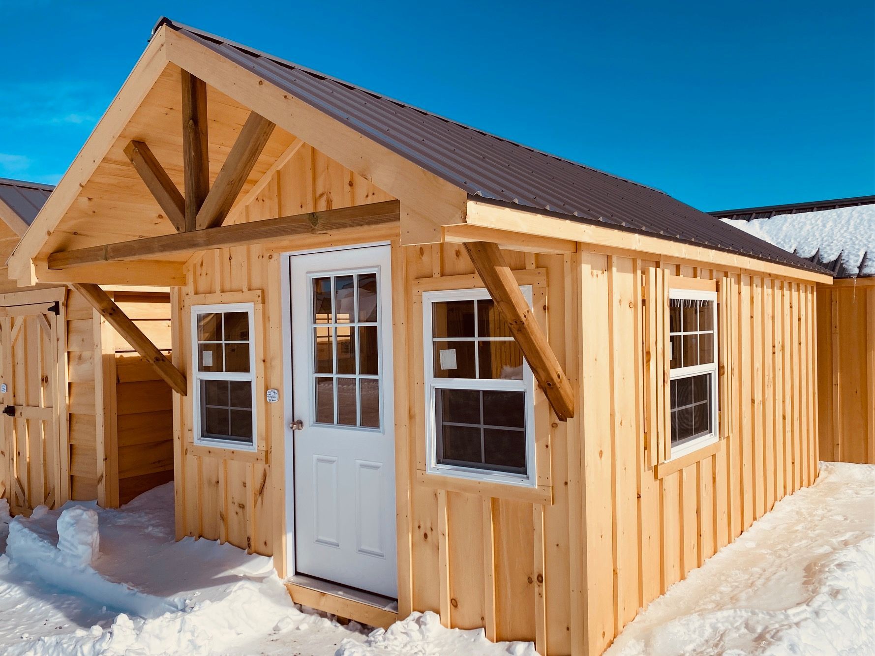 Wooden shed with metal roof, snow on the ground, and a blue sky.