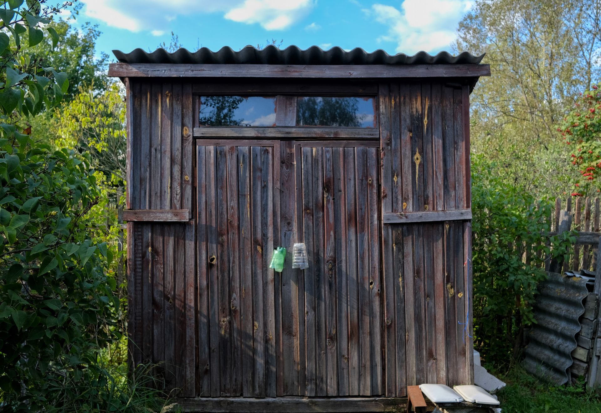 Small weathered wooden shed with a corrugated roof, set in a lush garden area