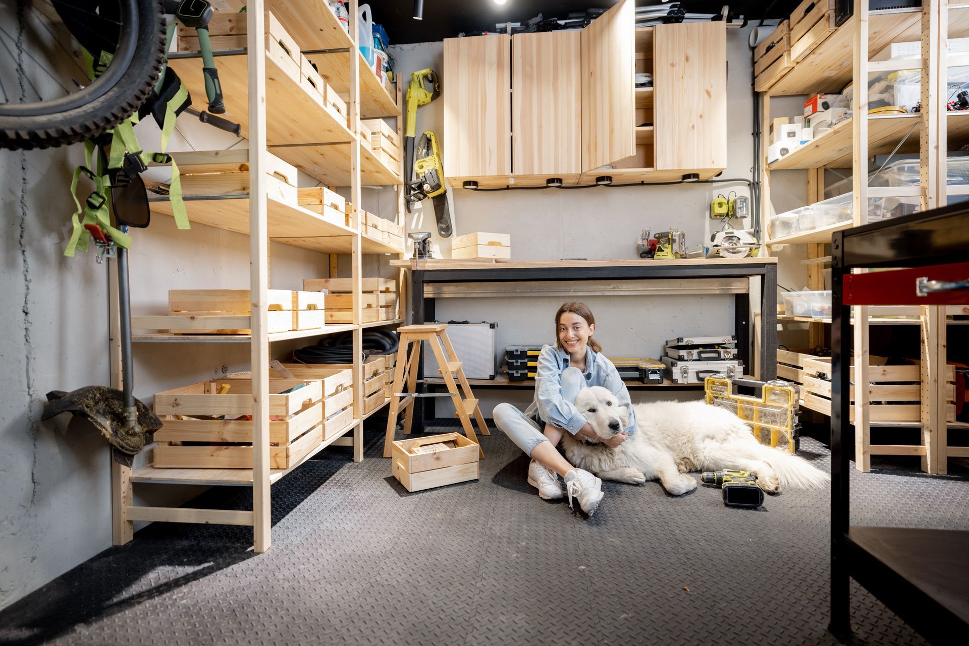 Woman sitting on the floor hugging a large white dog in a modern, organized workshop