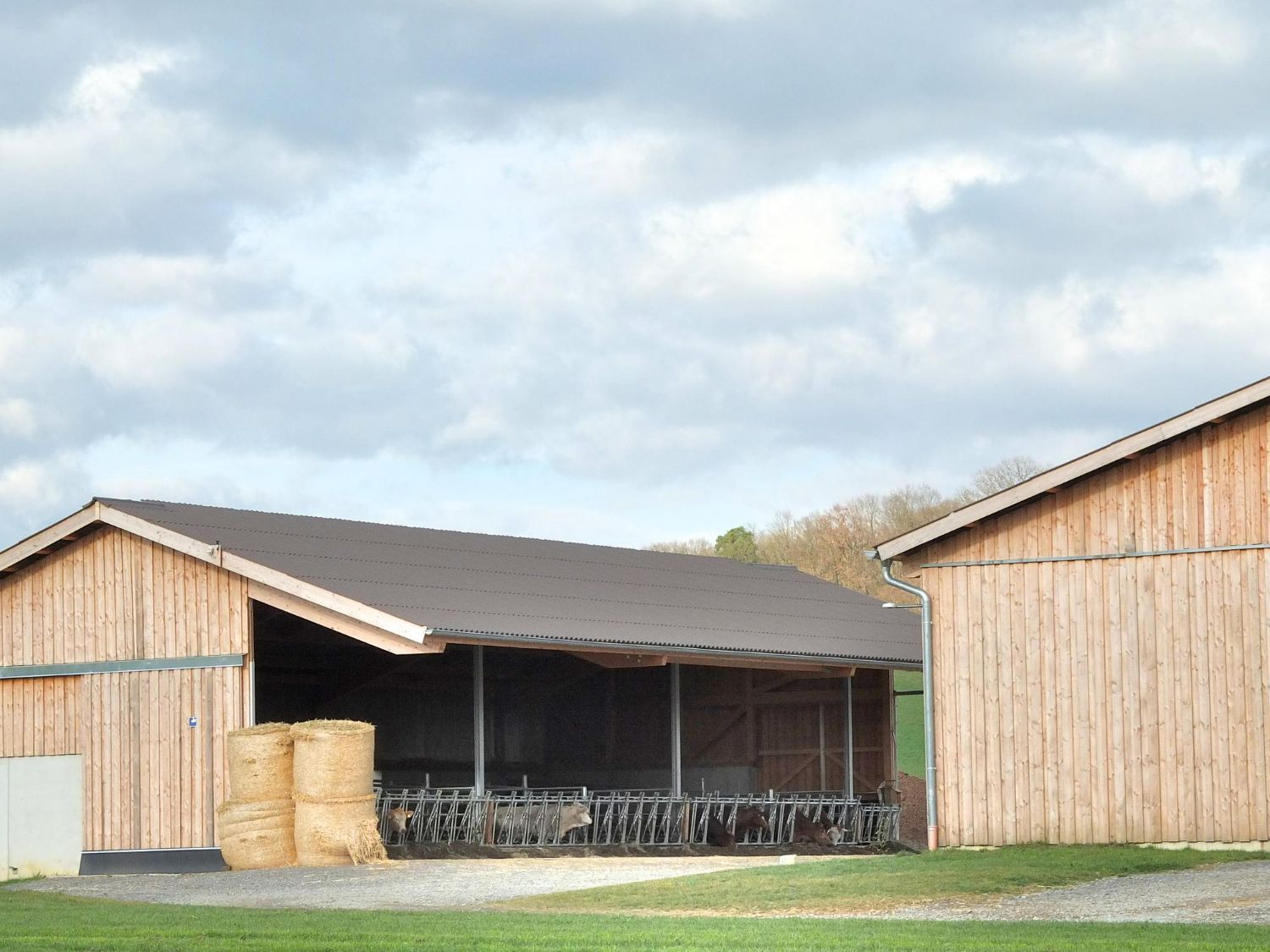 Two wooden barns with hay bales and bicycles under a cloudy sky