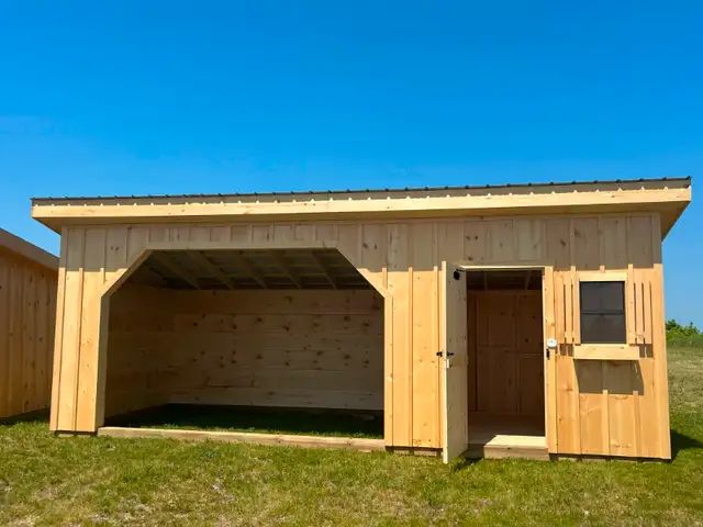 A wooden shed with the door open is sitting in the middle of a grassy field.