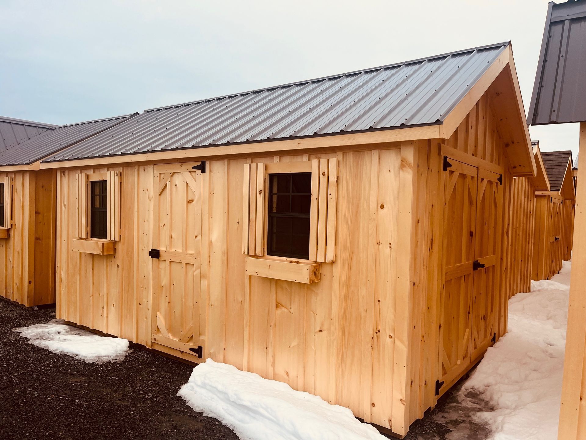 Wooden shed with metal roof and two small windows, outdoors.