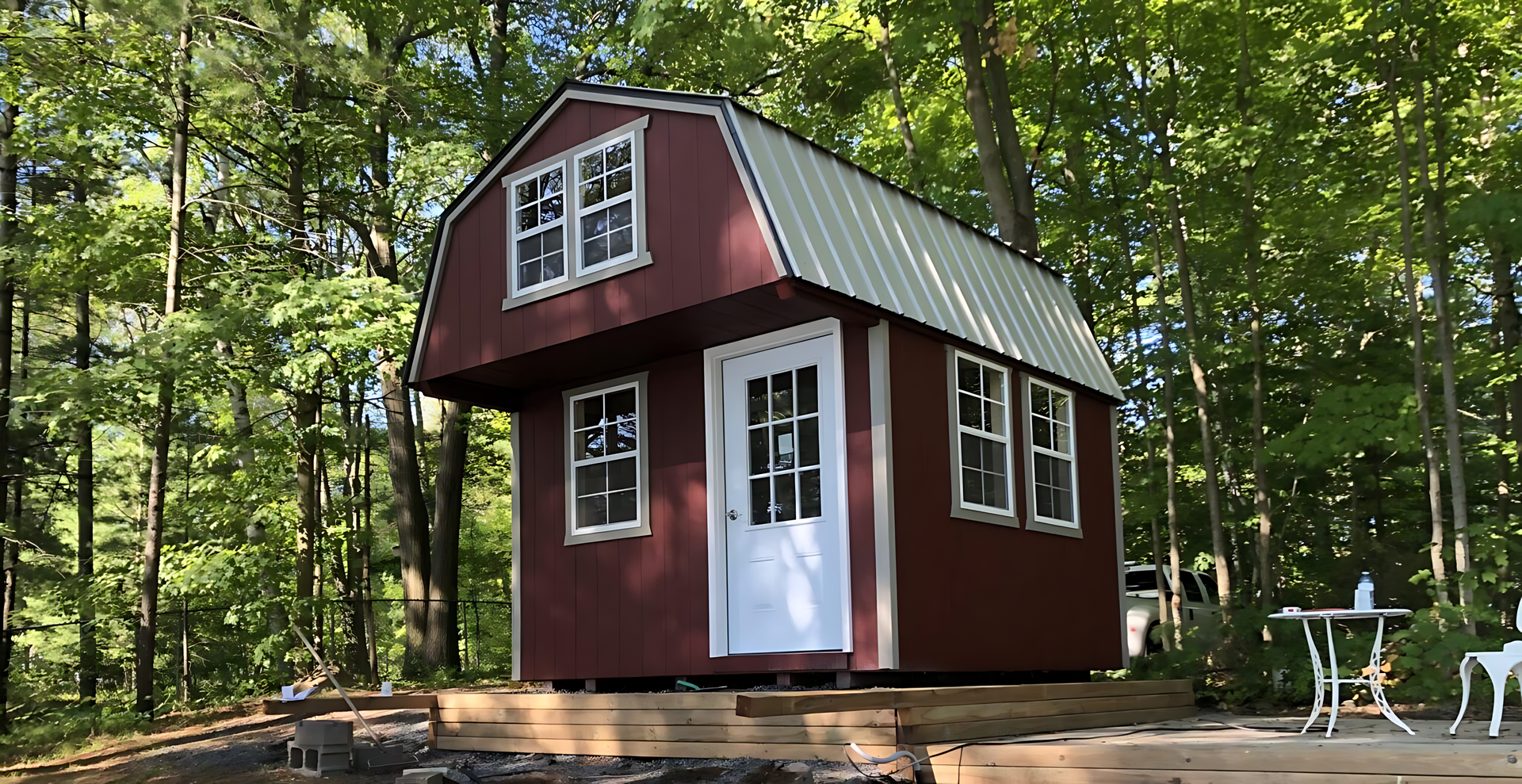 A small red barn with a white door and windows is sitting in the middle of a forest.
