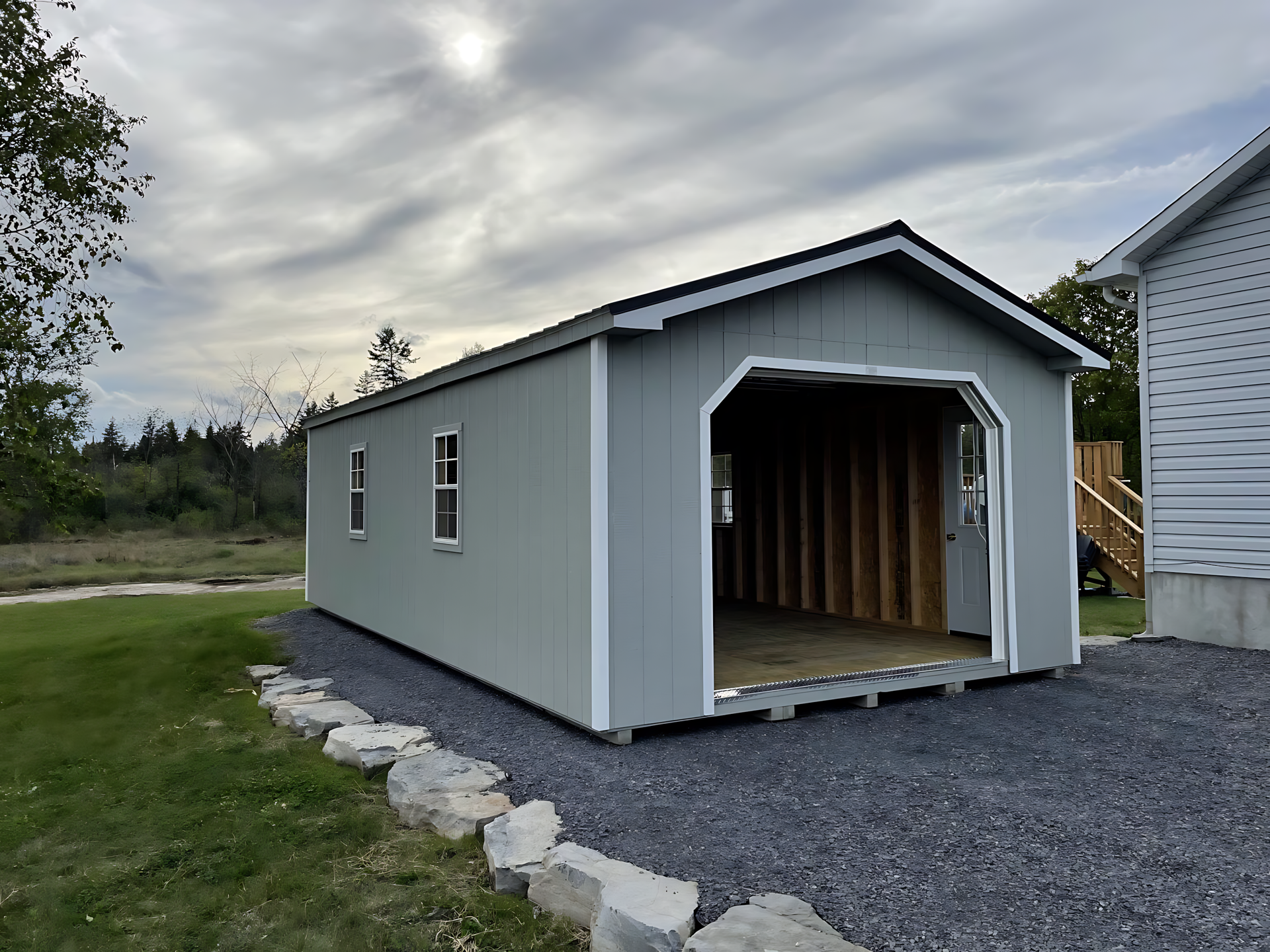A gray garage with the door open and a house in the background.
