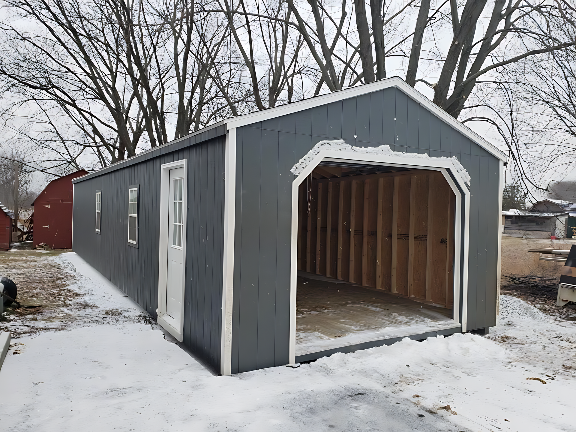 A gray garage with a white trim is sitting in the snow.