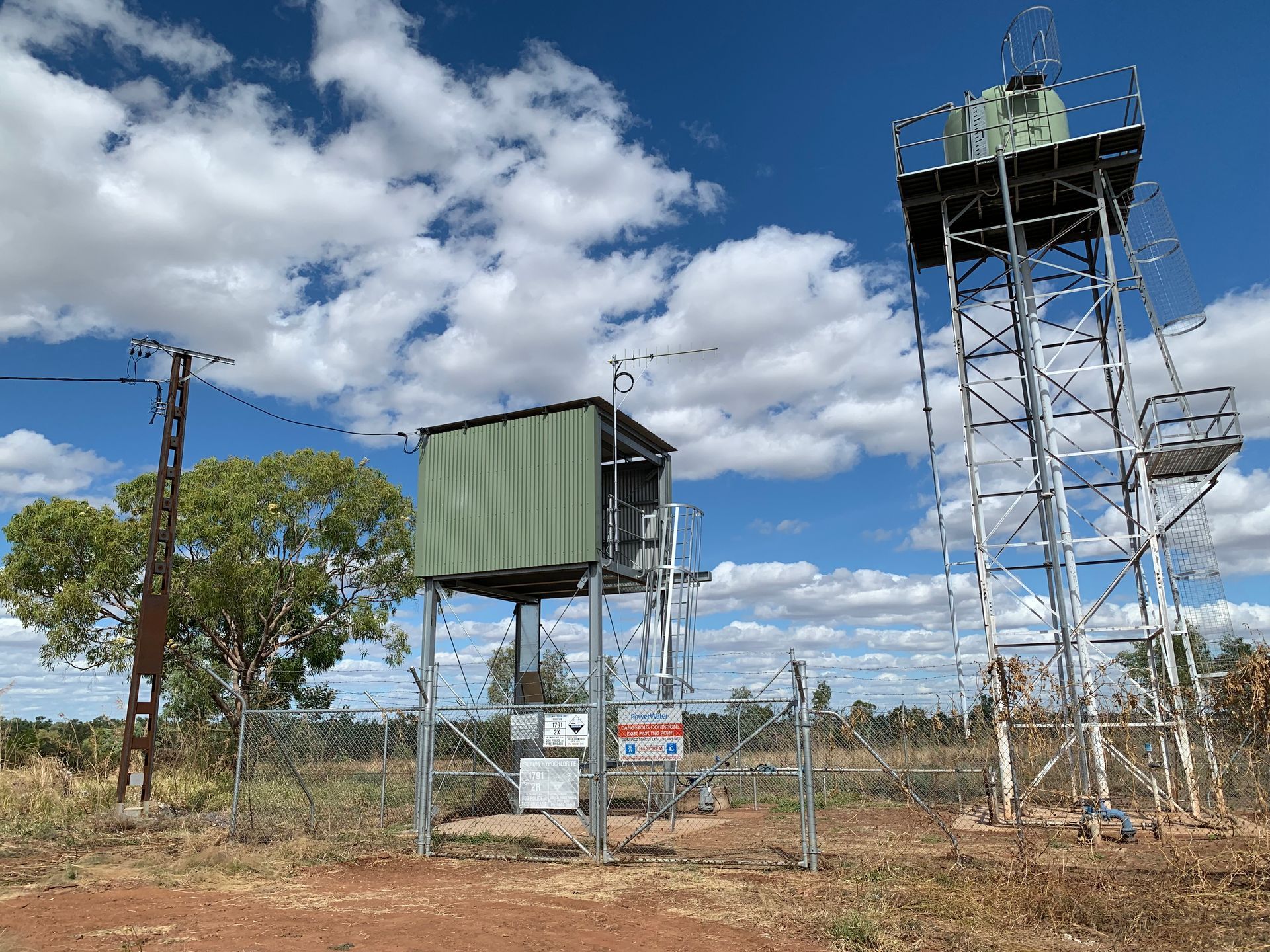 A green water storage structure is behind a security fence — CCD Electrical In Berrimah, NT