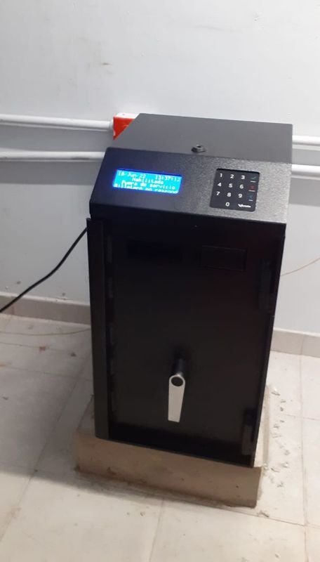 Una caja fuerte negra está sobre un suelo de baldosas al lado de una pared.