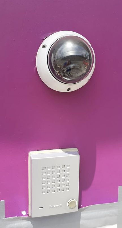 Una cámara de seguridad está montada en una pared violeta al lado de un timbre.