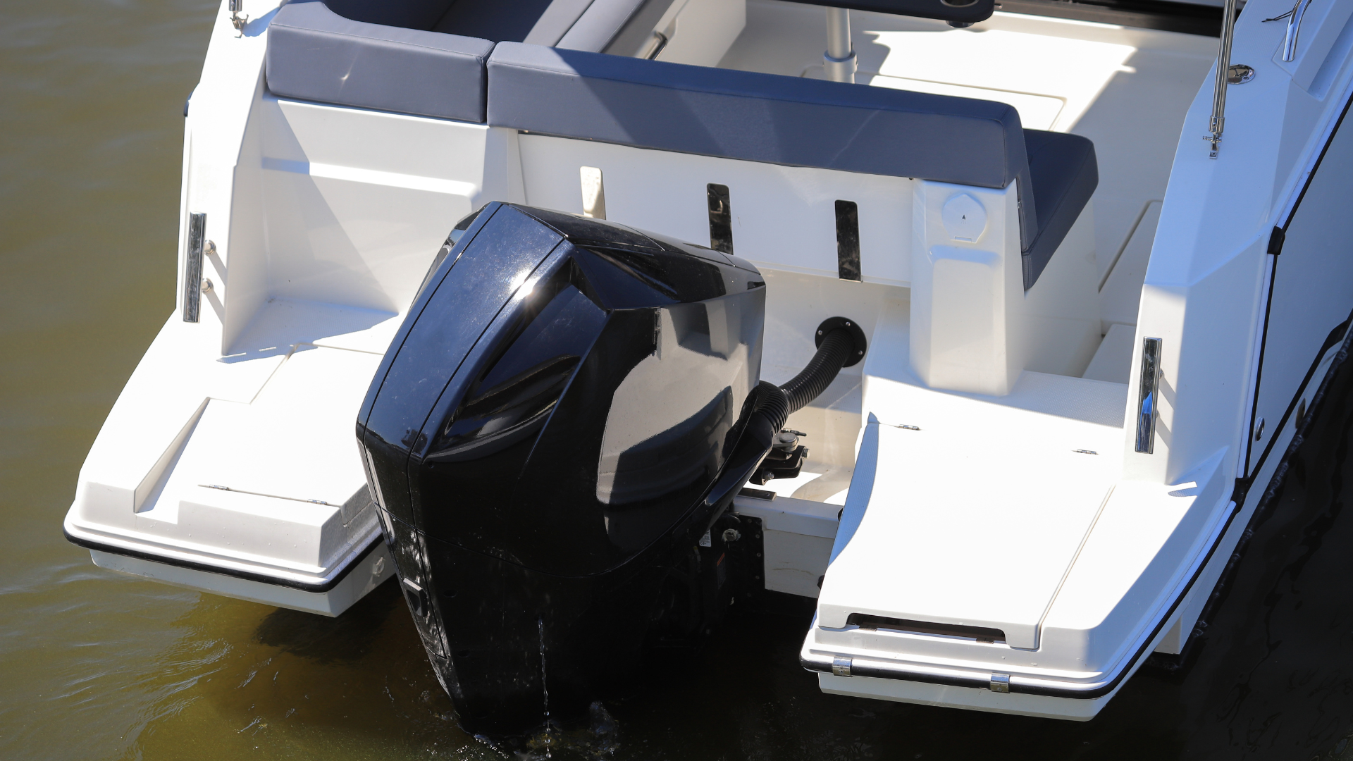 A white boat is parked on the side of the road in front of trees.