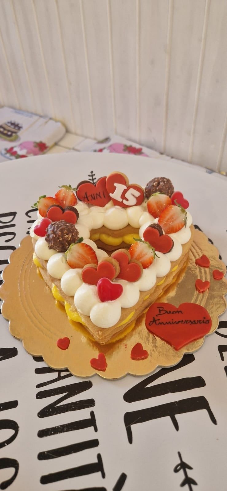 Torta a forma di cuore decorata con fragole e panna, su un centrino dorato con la scritta