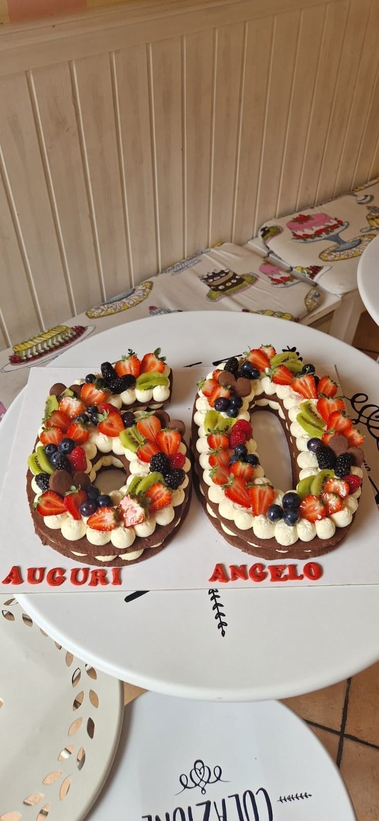 Torta a forma di numero 60, decorata con frutta, su un vassoio bianco, con la scritta
