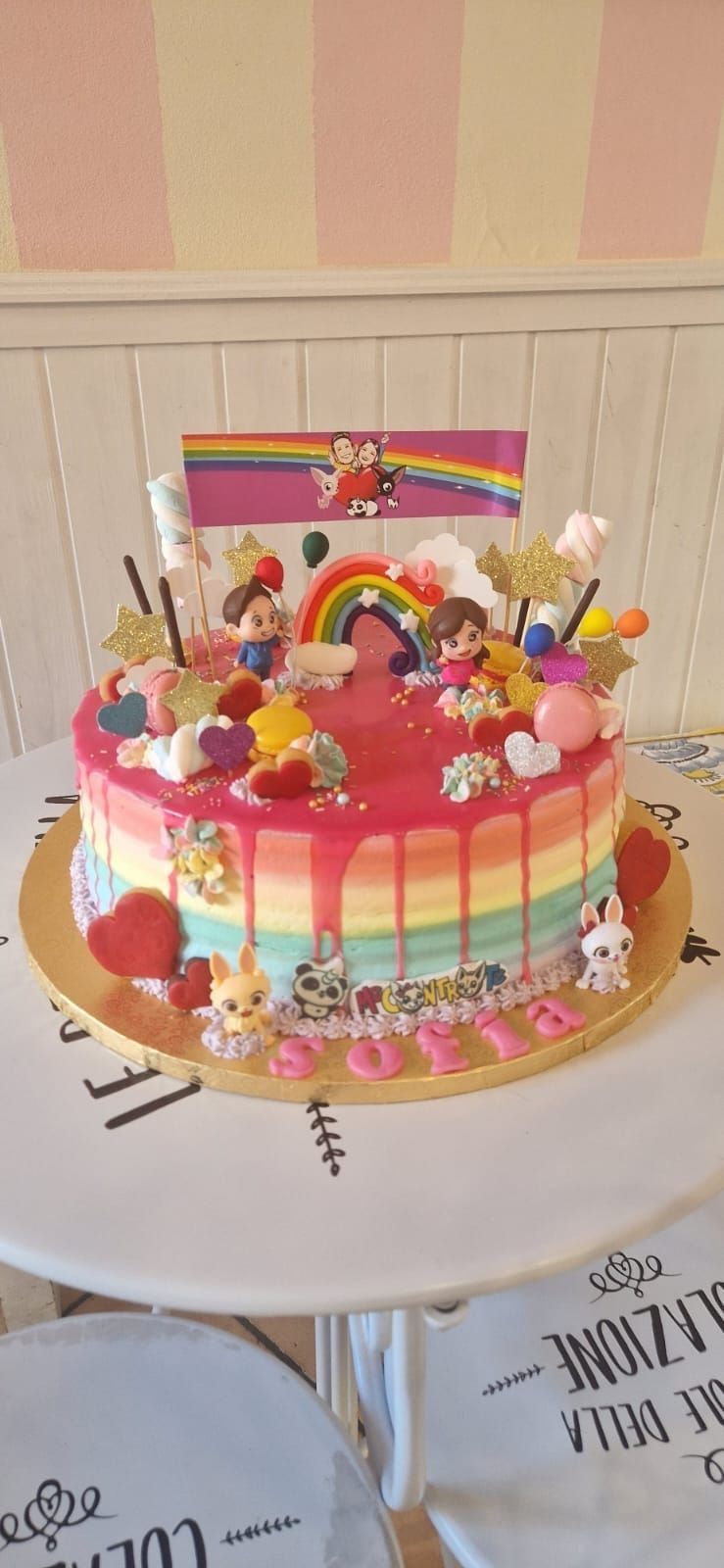 Torta di compleanno colorata decorata con personaggi dei cartoni animati e arcobaleno.