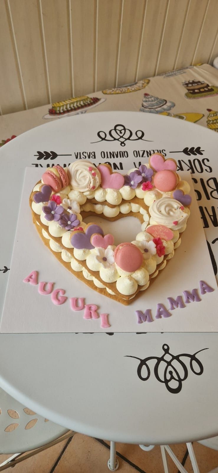 Torta a forma di cuore decorata con crema, fiori e macarons, con la scritta
