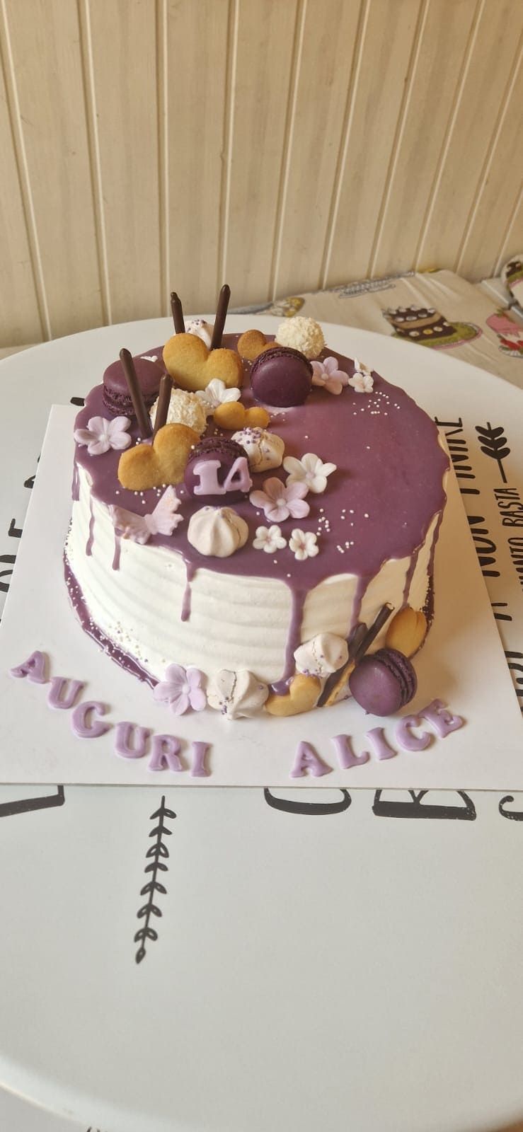 Torta di compleanno con glassa viola, decorata con macarons e fiori; sopra è scritto