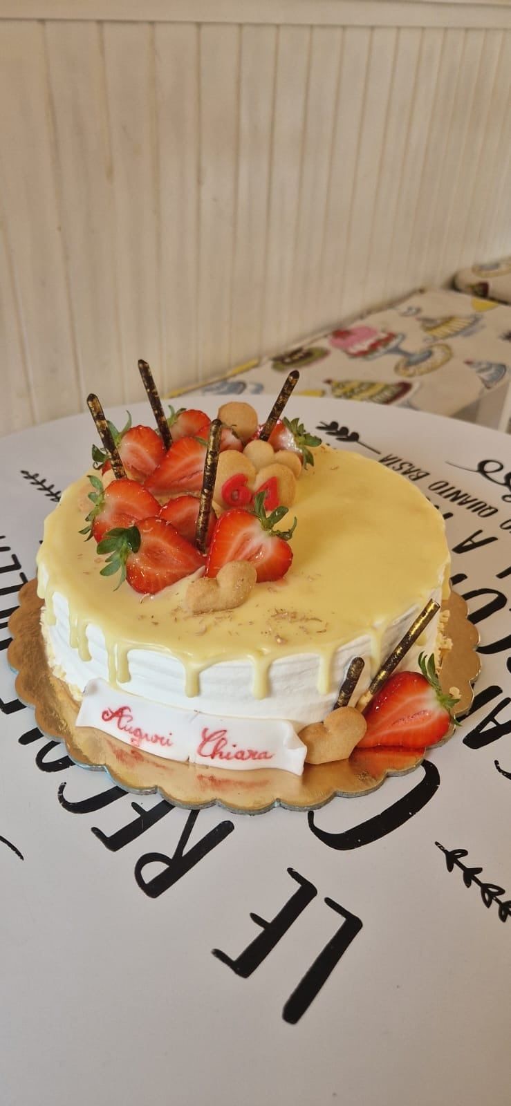 Una torta decorata con fragole e bastoncini di cioccolato su una base dorata, adagiata su una superficie decorata.