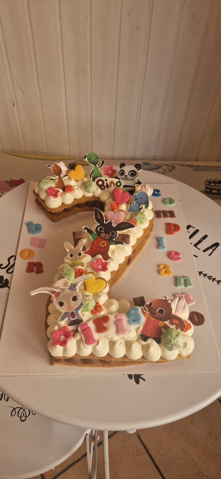 Una torta a forma di numero 3 decorata con panna, caramelle e giocattoli su un piatto bianco.