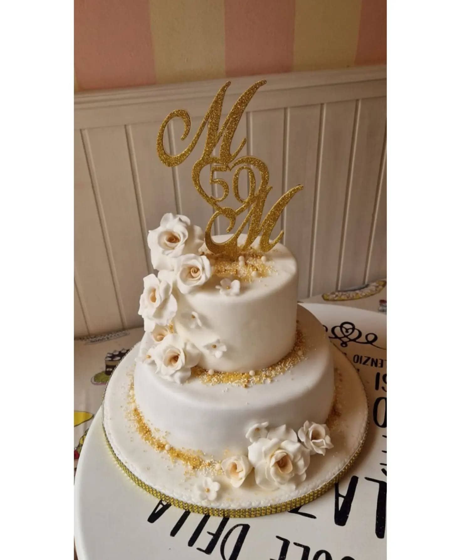 Torta bianca a due piani con dettagli dorati e fiori; decorazione