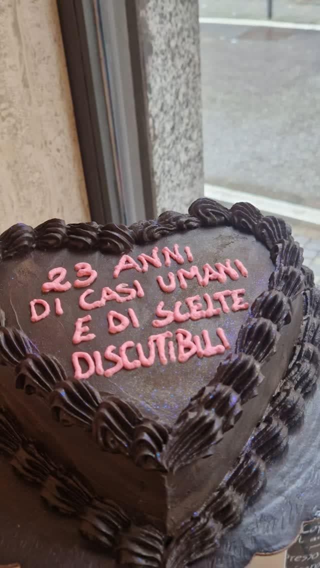 Torta al cioccolato a forma di cuore con glassa rosa. Il testo recita: