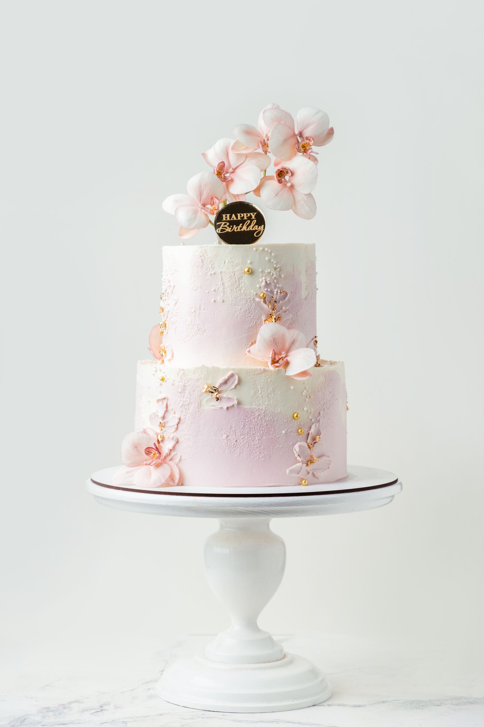 Torta a due piani rosa e bianca con decorazioni di orchidee su un'alzata bianca.