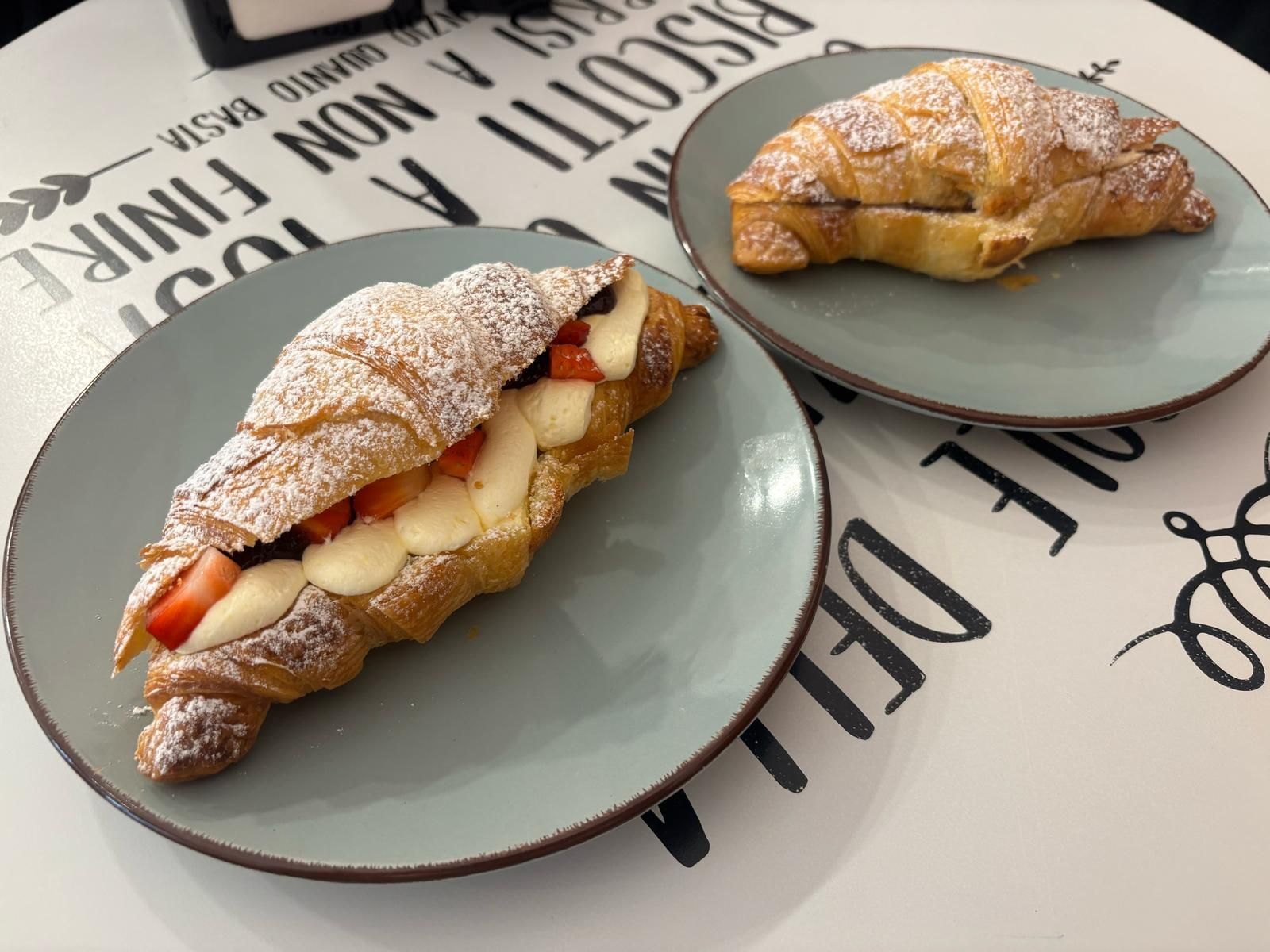 Due croissant su piatti: uno ripieno di crema e fragole, l'altro di cioccolato, su un tavolo decorato.