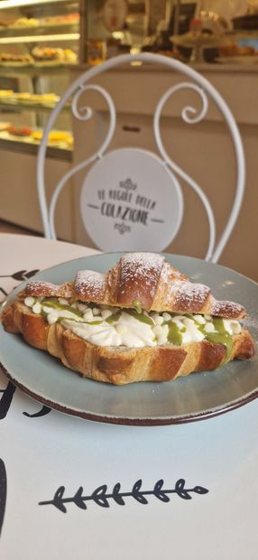 Cornetti ricoperti di cioccolato, noci e frutti di bosco esposti su uno scaffale di vetro.