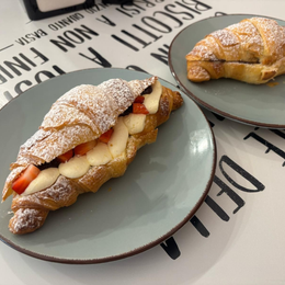 Cornetti ricoperti di cioccolato, panna, frutti di bosco e pistacchi esposti in una panetteria.