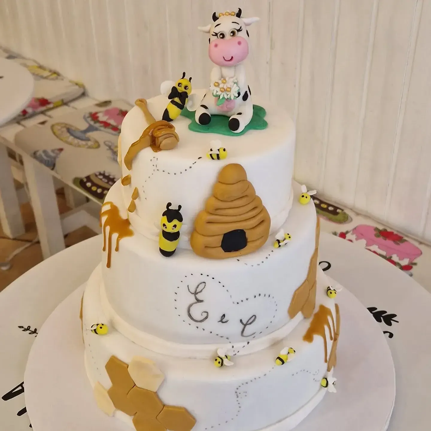Torta a tre piani decorata con una statuina di mucca, api, un favo e gocce di miele.