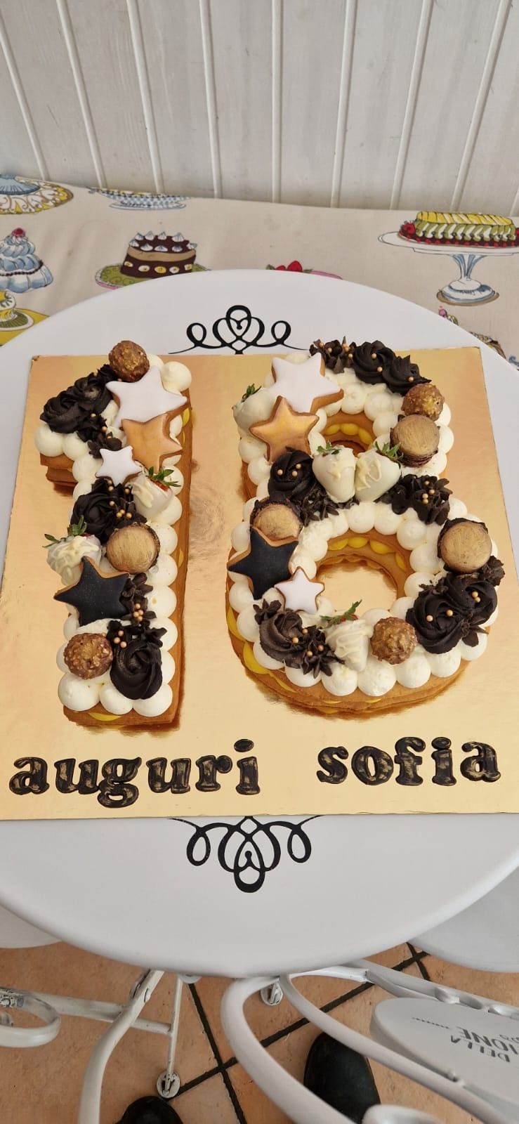Torta di compleanno a forma di "18", decorata con glassa bianca, cioccolatini e "Auguri Sofia".