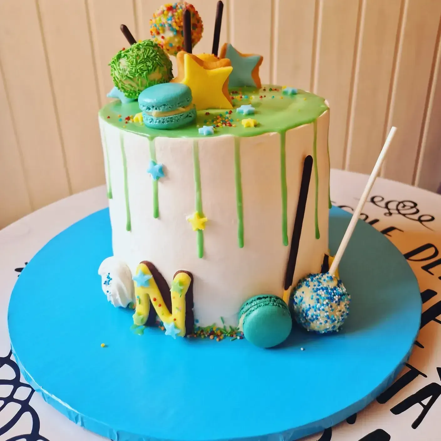 Torta decorata con gocce di glassa verde, macaron, stelle e una