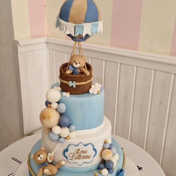 Torta a tre piani con tema mongolfiera e orsacchiotto, prevalentemente blu e bianco.