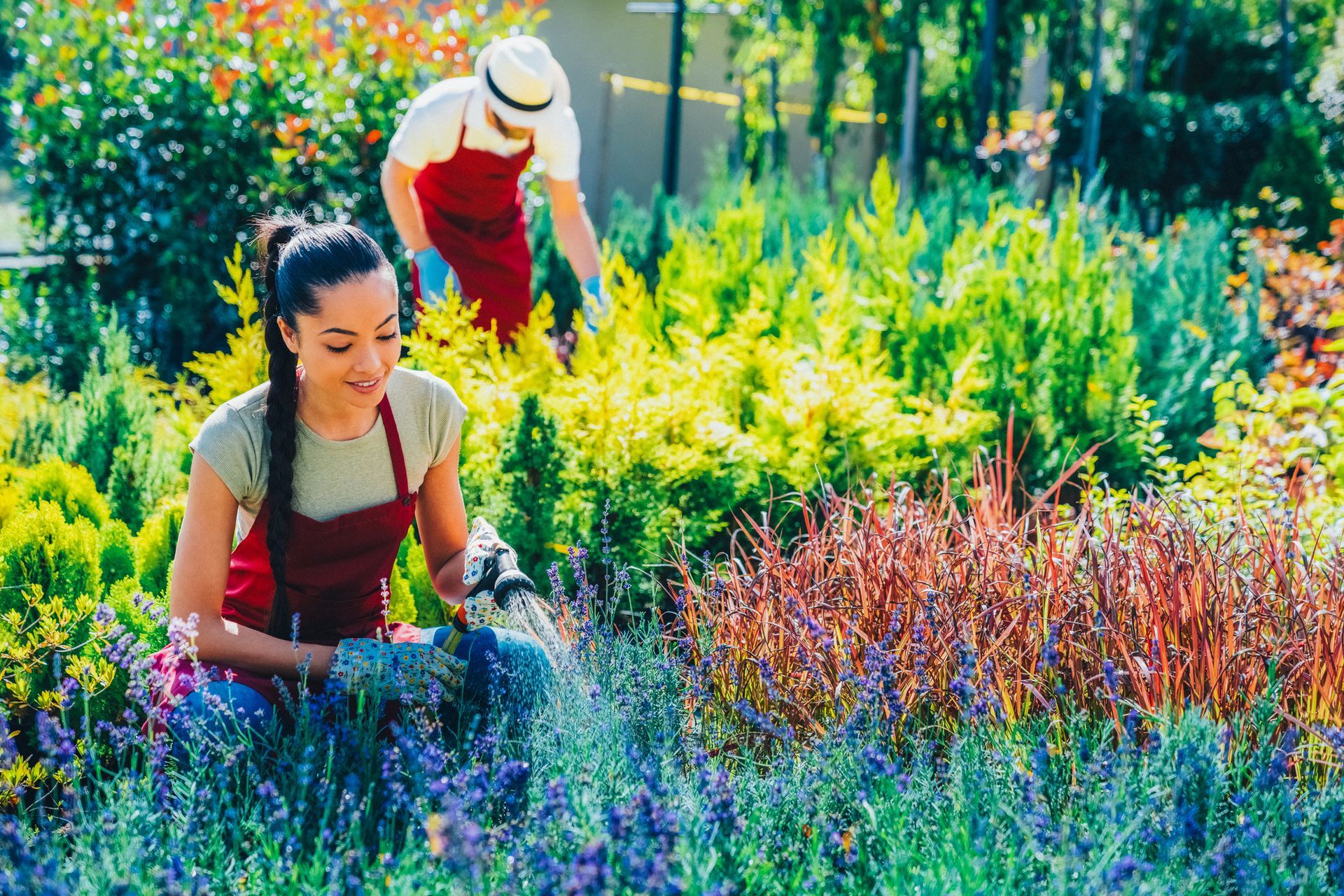 A man and a woman are watering plants in a garden.