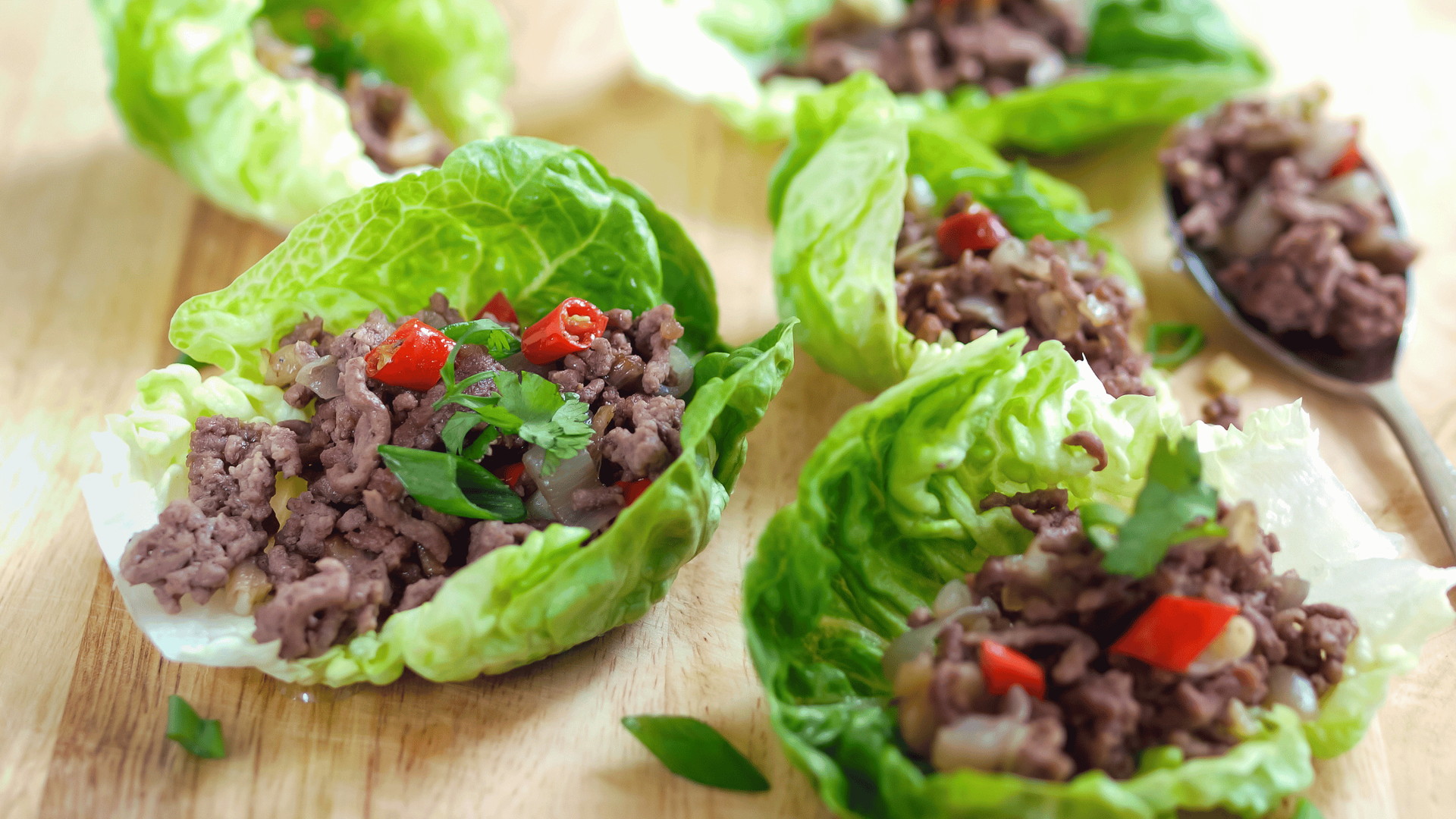 Fresh lettuce wraps filled with beef and vegetables on a wooden cutting board.