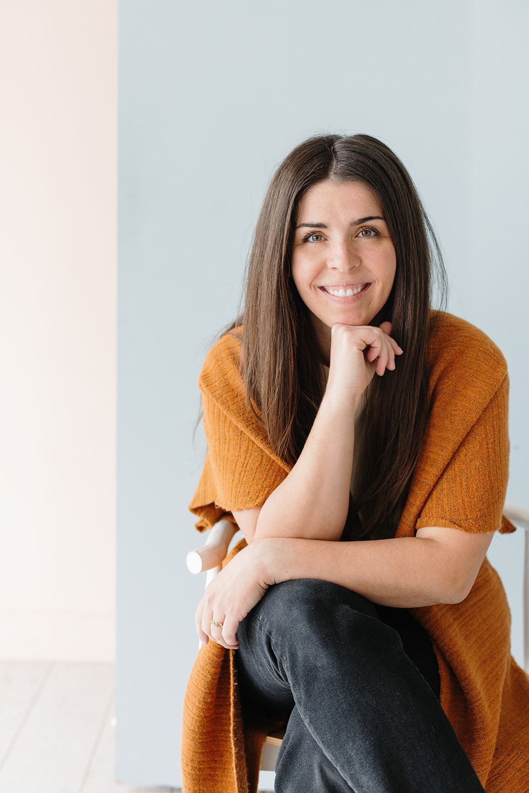 Lucia Killian smiling at the camera in a rust-colored sweater, seated with a relaxed and friendly expression.