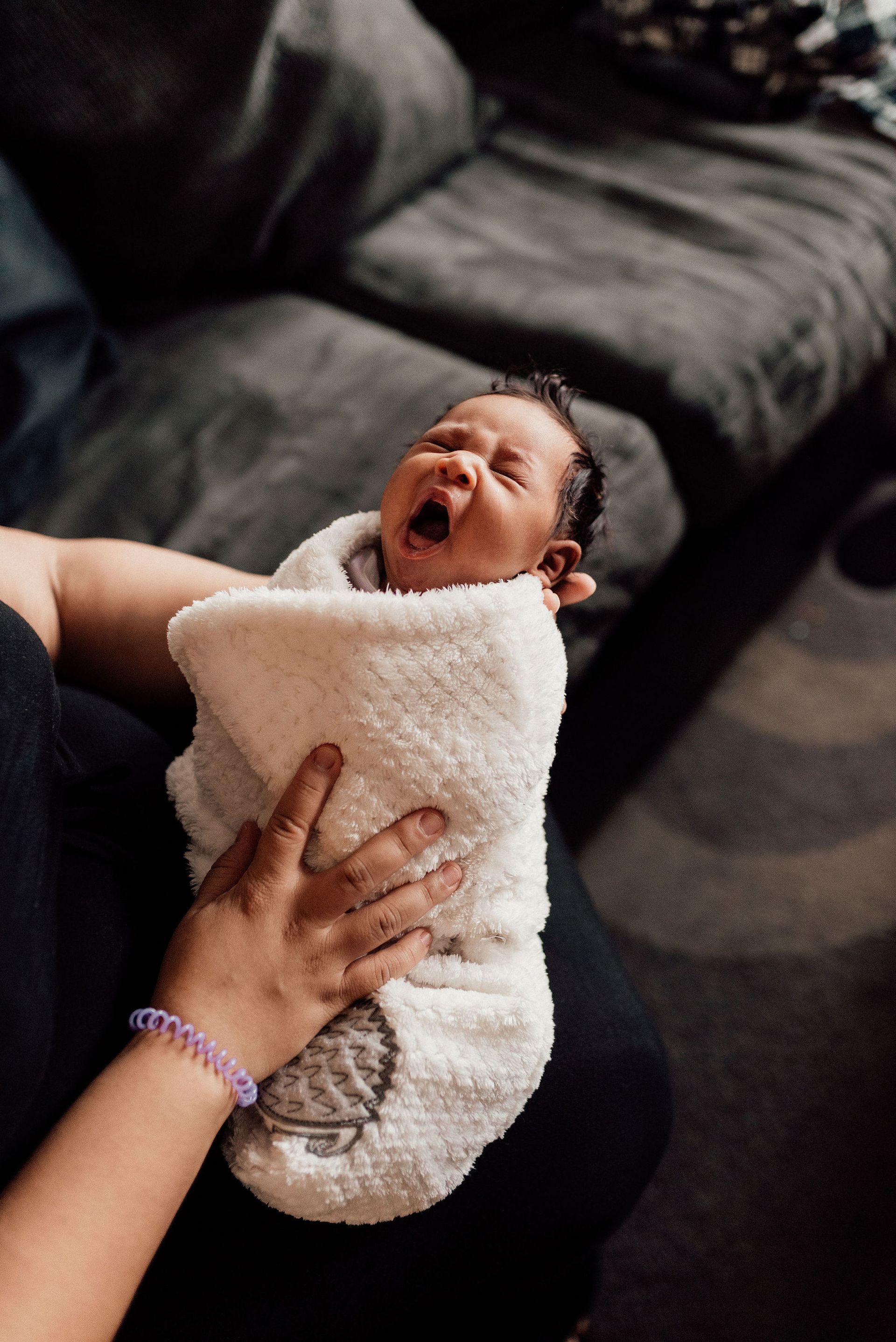 Yawning newborn wrapped in a white towel during postpartum nighttime care.