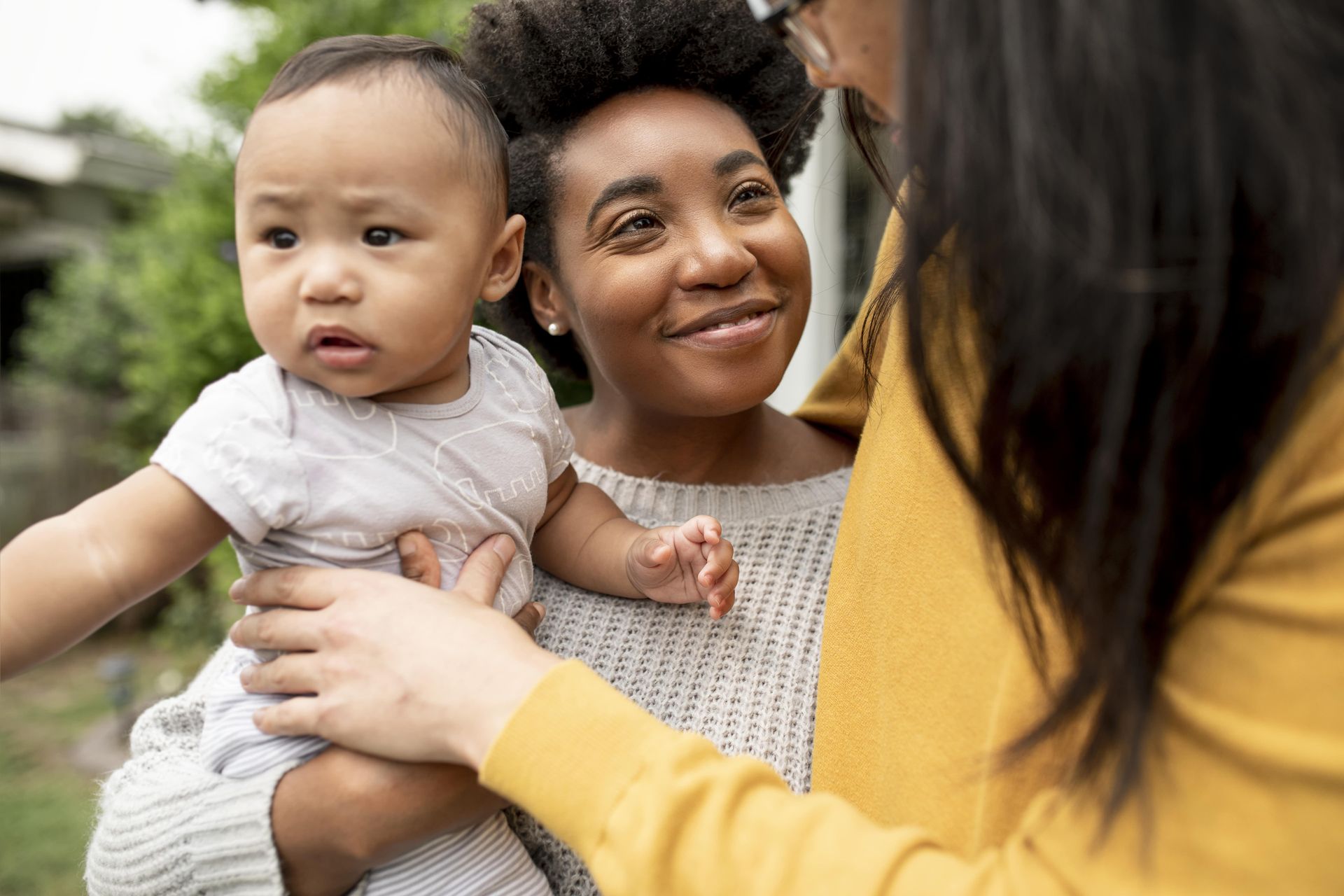 A smiling woman holds a baby, gazing warmly at another person.