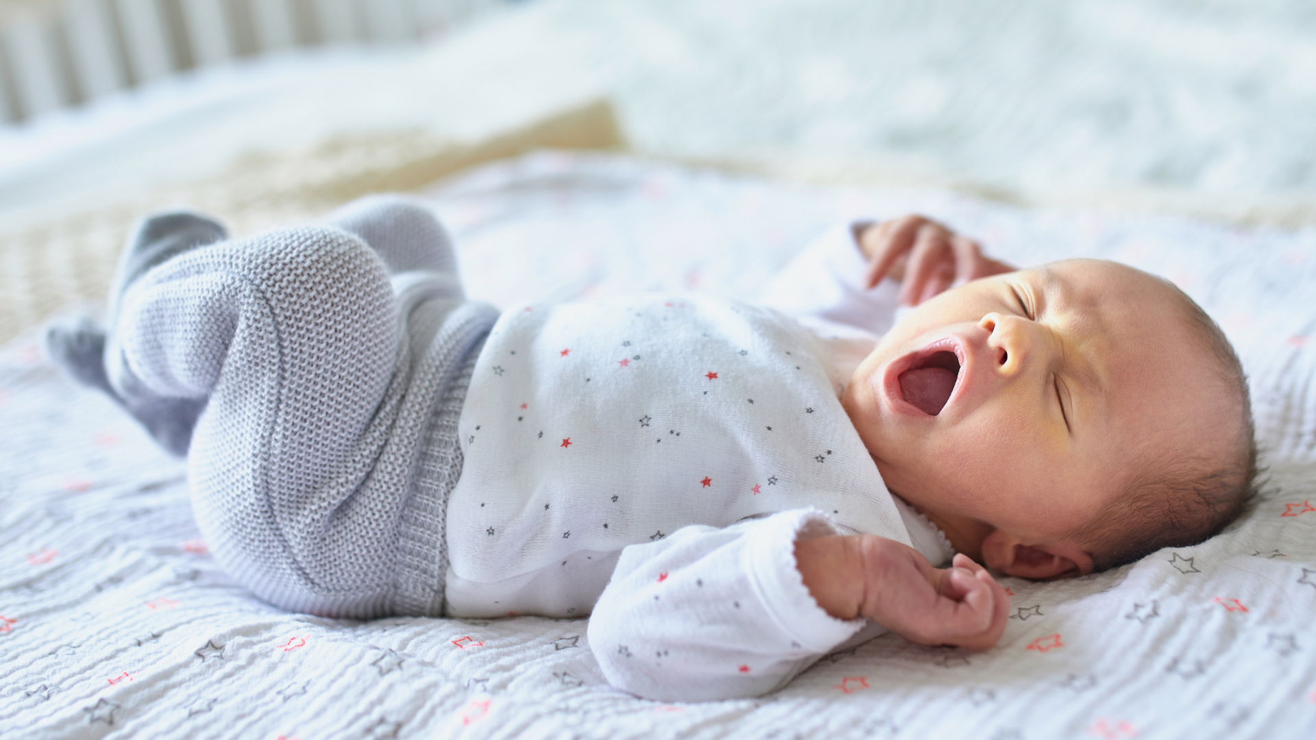 a newborn laying in bed and yawning