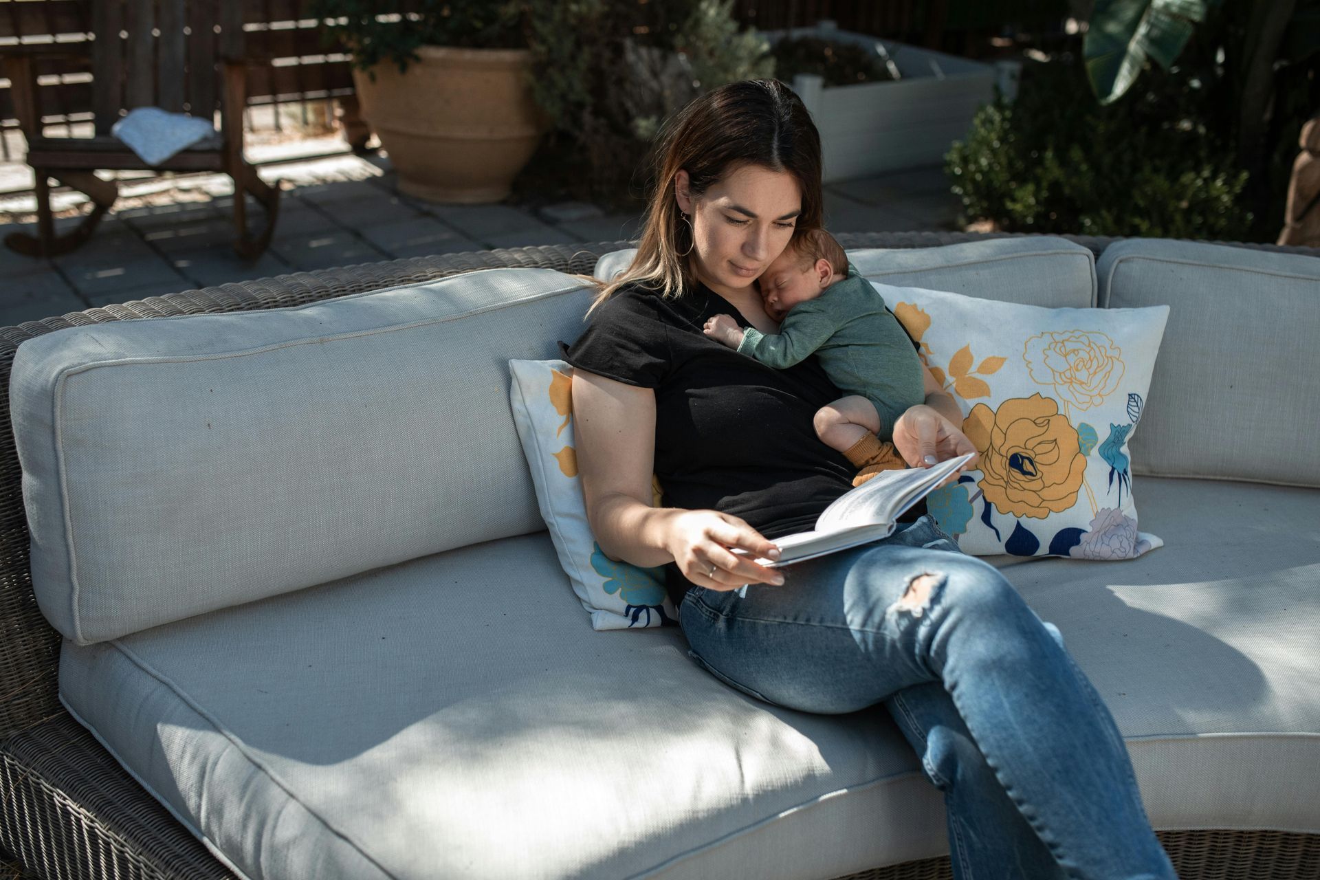 new mom reading a book while holding newborn baby