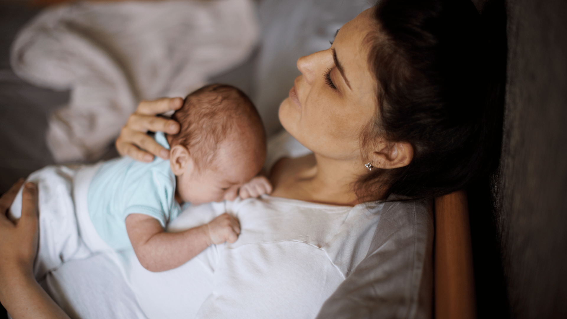 A serene scene of a mother resting on her side, eyes closed, gently cradling her sleeping newborn.