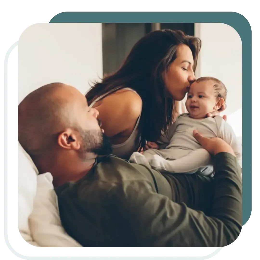 Smiling parents cuddling their newborn baby at home, showing the warmth, care, and bonding that postpartum doulas and night nannies provide for Utah families.