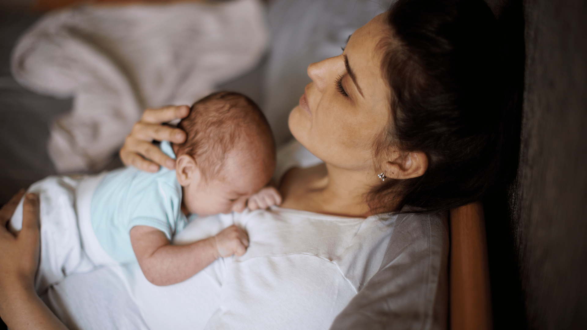 A mother lies in bed, lovingly holding her newborn baby, capturing a serene moment of motherhood.