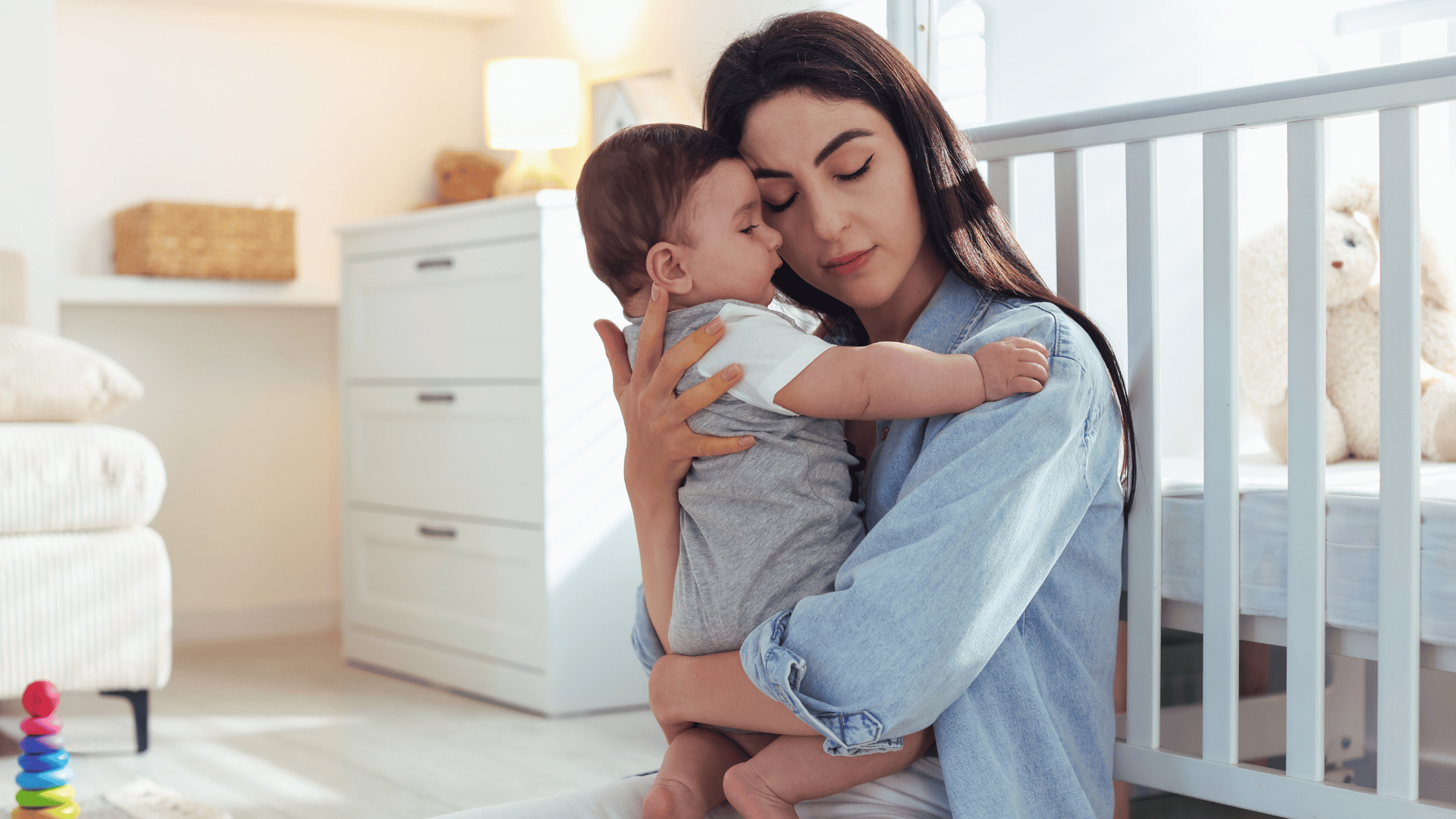 A woman lovingly cradles a sleeping baby in a cozy nursery.